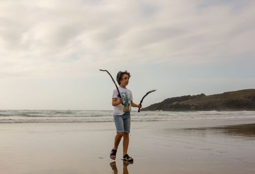 boy with sticks in his hands is walking in a cloudy day in August