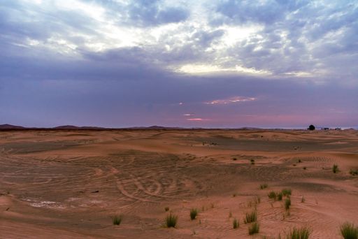 A beautiful shot of vast land with tire tracks on the sand with an indigo clouds background