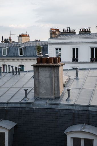 The zinc rooftops with TV antennas and a group of chimneys under cloudy sky in Montmartre, Paris, France