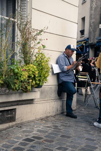 A street artist leans his back against a building, drawing someone portrait in the street in Paris, France