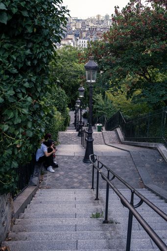 A vertical shot of two people sitting on the stairs leading to The Basilica of the Sacred Heart of Paris, France