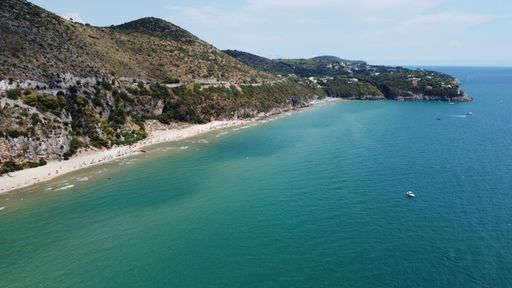 A landscape of hills covered in greenery surrounded by the sea under a blue cloudy sky