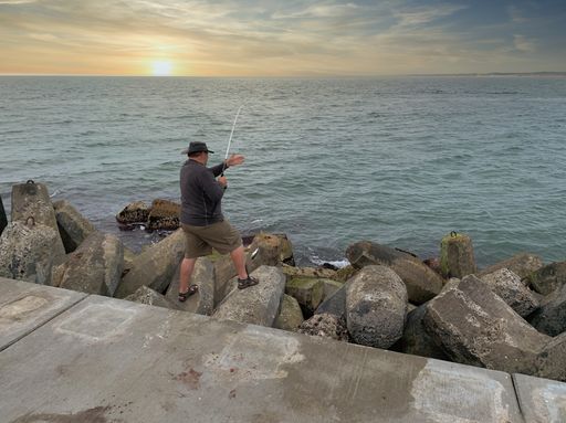 A fisherman fishing in the ocean under the sunset