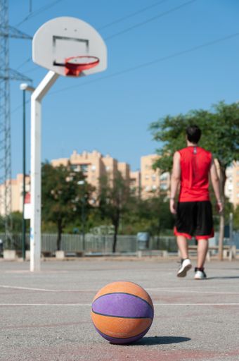 A vertical selective focus shot of a basketball in a court with the male player walking near the ring
