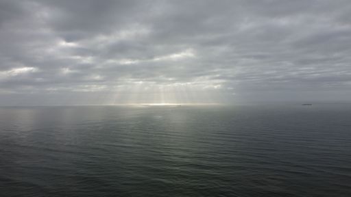 An aerial view of distant sun rays in the cloudy sky shining on the sea water