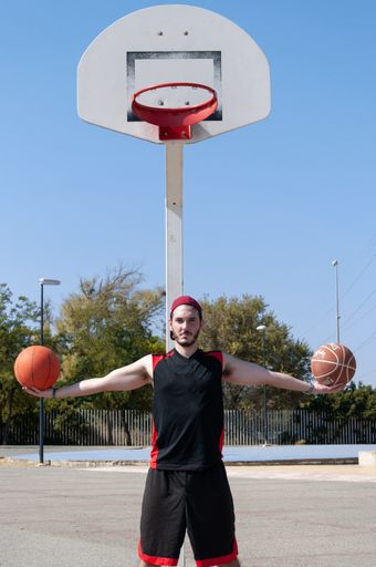A vertical shot of an athletic man holding basketball balls