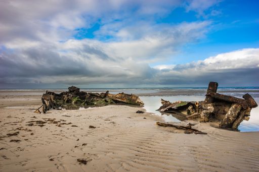 An old shipwreck boat stuck in the beach sand against a blue sky background with soft clouds