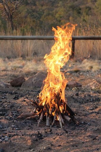 A vertical shot of a campfire on the rocky ground in the daylight
