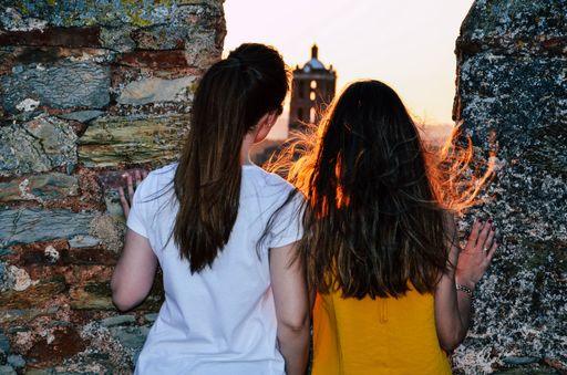 A back view of the two young ladies standing next to the stone fence with a golden sunset background