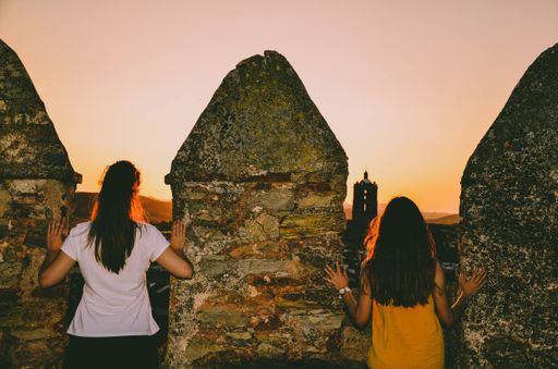 A back view of the two young ladies standing next to the stone fence with a golden sunset background