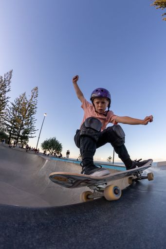 A vertical shot of a kid wearing a helmet doing tricks on a skateboard in a park
