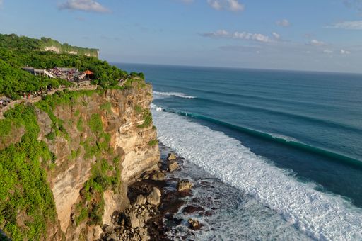 A high-angle shot of a rocky shore with sea waves and the Uluwatu Temple on a high cliff, Indonesia
