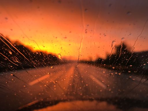 The raindrops on the front window of a car riding through a highway at sunset
