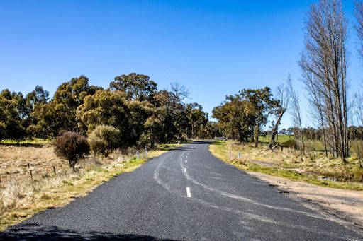 An bitumen country road through brown fields at Emmaville, New South Wales, Australia under blue sky