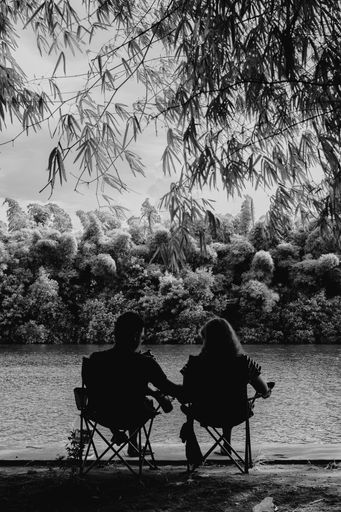 A vertical shot of a beautiful couple sitting near the lake