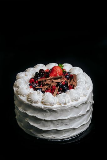 A vertical top view of a birthday cake with cream decorated with berries and on a black background
