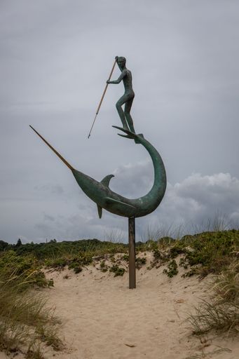 A metal sculpture of a harpooner on the beach