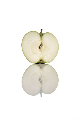 A vertical shot of a half green apple on a reflecting white surface