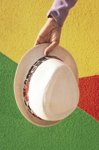 A vertical shot of female's hand holding a hat against a colorful wall background