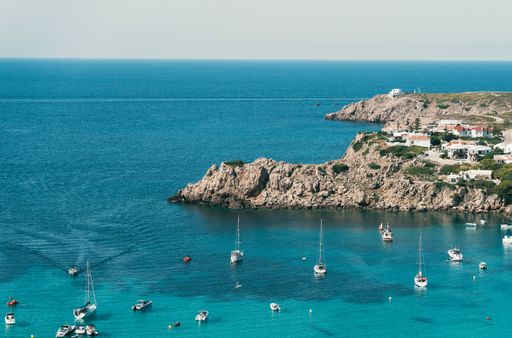 A beautiful Mediterranean sea view with small boats and a rocky shore with houses in Menorca island, Spain
