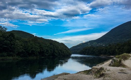A river surrounded by hills covered in greenery under a blue cloudy sky