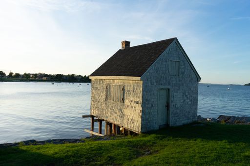 A calm scenery of a brick summerhouse near the shore of a lake under a clear sky