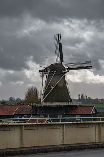 A vertical shot of an old windmill against dark cloudy sky background