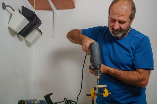 bearded man carpenter craftsman drilling wood with an electric drill in his woodworking shop