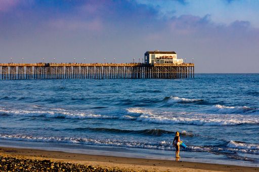 A little girl at the beach near a harbour and the wooden dock in the wavy ocean, on a sunny day