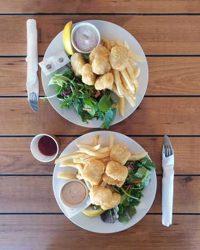 high angle view of two plates of battered fish cocktails served with fries and salad on wood table