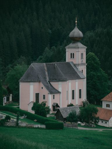 A vertical shot of a parish church of St. Ulrich with a forest background