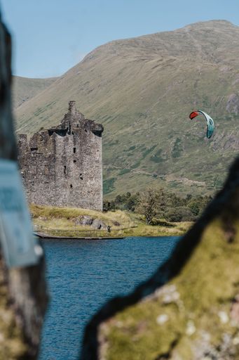 A vertical shot of the ruins of historic Kilchurn Castle with a kitesurfer floating nearby in Scotland