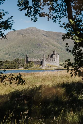 A vertical of the historic Kilchurn Castle ruins with mountains in the background