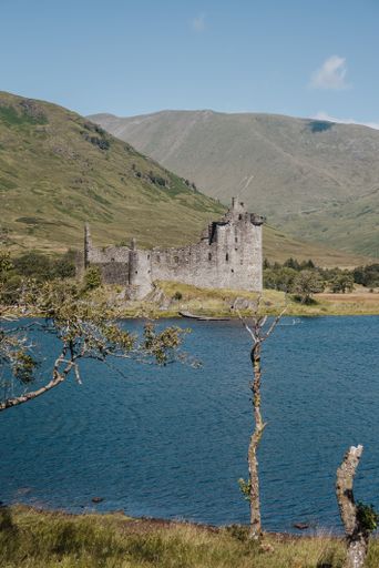A vertical of the historic Kilchurn Castle ruins near a blue lake with mountains in the background