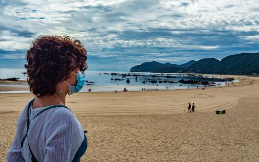 A young female in a medical mask enjoying a view of the ocean
