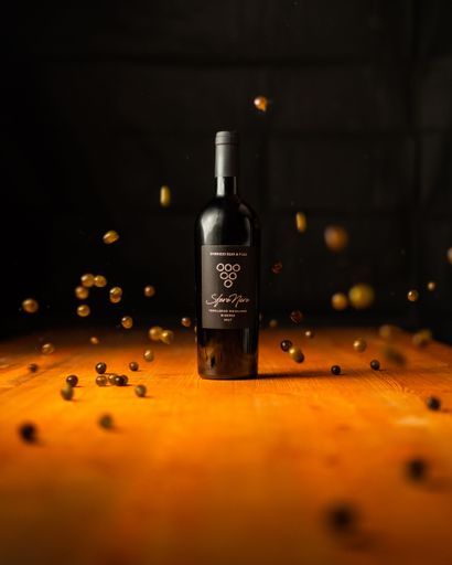 A Sfere Nere red wine bottle on a wooden table with scattered grapes