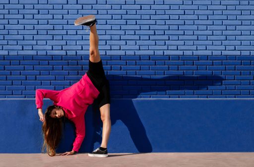 A Caucasian woman dancing urban dance with daylight and a blue background