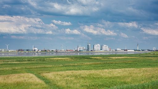 A scenic view of a green field and river on the background of buildings under the cloudy sky