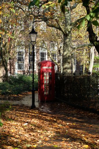 A vertical shot of the red phone booth in a park in London on ana autumn day
