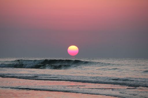 A beautiful scenery of black sea waves at sunset with a bright pink moon in the sky