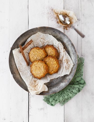 A vertical high angle shot of delicious cookies with cinnamon in a metal bowl and a spoon on a white wooden surface