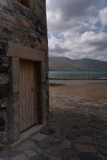 A vertical closeup shot of a small wooden door on the cost of an ocean with hills in the background