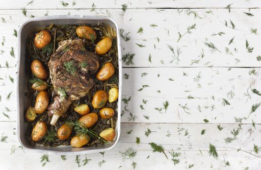 A high angle shot of steak with seasonings and potatoes on a white wooden table covered with green leaves