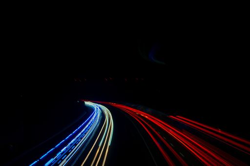 A long-exposure shot of car headlights and tail lights on a dark road during nighttime