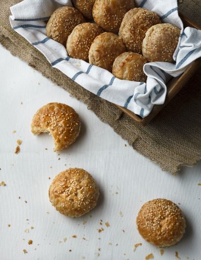 A high angle shot of a bitten croquette near a basket full of homemade croquettes on a white table covered with crumbs