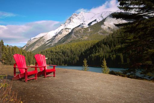 Two red wooden chairs on the lakeside with densely forested hills background