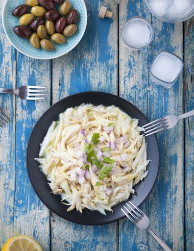 A vertical high angle shot of tagliatelle pasta in a black plate near a plate of olives on a wooden table
