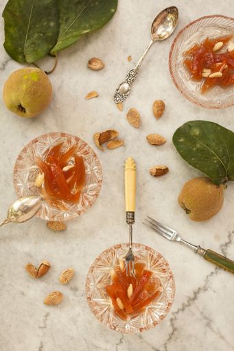 A high angle shot of glass bowls with quince jam and almonds on a white surface