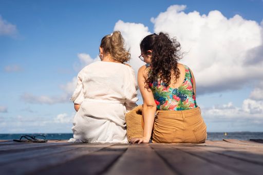 Mother and daughter sitting on the pier of the port of Barra facing the sea in Salvador, Brazil