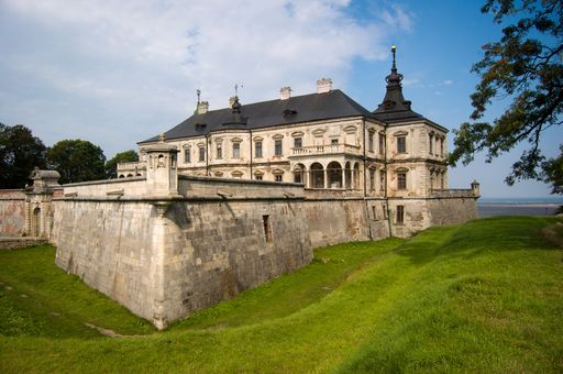 The Pidhirtsi Castle in a field covered in greenery under a blue cloudy sky in Ukraine